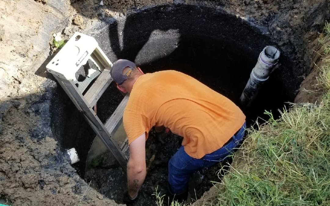 Godley Septic technician inside an open septic tank pit, working alongside the pump and outlet pipe — real pumping and cleaning service